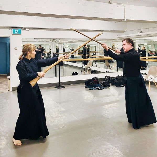 Two jūkendō practitioners cross wooden training rifles during partner practice.