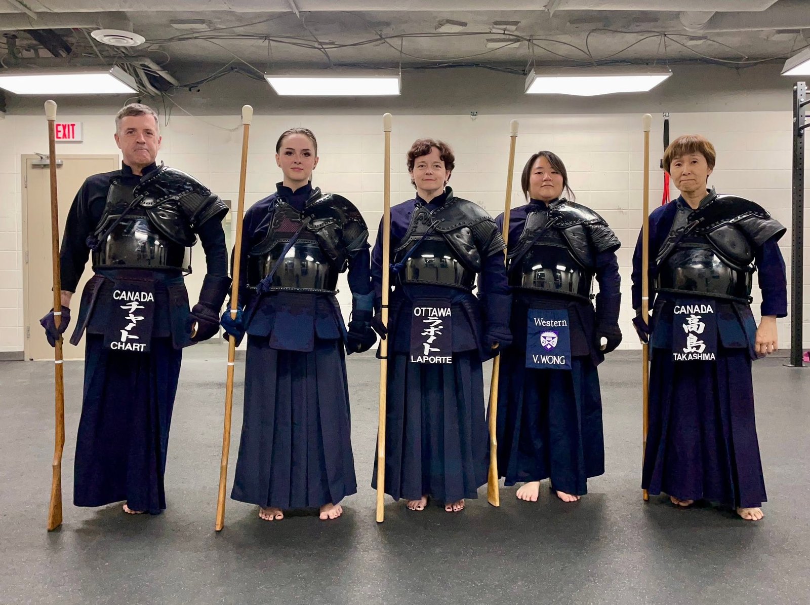 Five jūkendō practitioners stand together wearing protective armour and holding wooden training rifles.